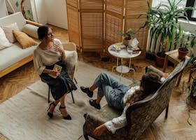 Two women engaged in a coaching session in a warm, inviting interior with plants and natural lighting.